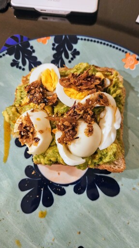 Smashed avocado on square piece of toast. Sliced hard-boiled egg on top, drizzled with crispy chilli oil. 