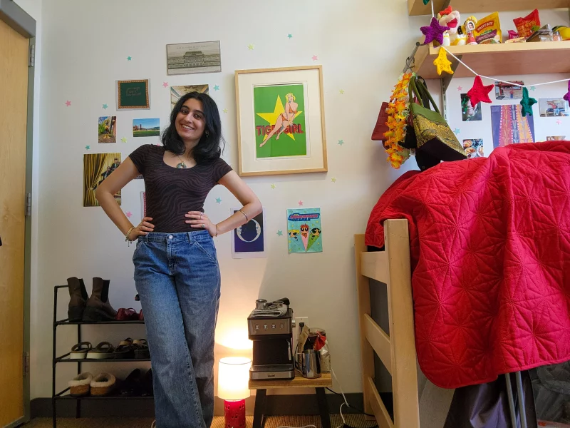 A picture of a young woman (second-year economics and human rights student Isha Mehta) in front of a Mel Ramos lithograph on the wall of her dorm room.