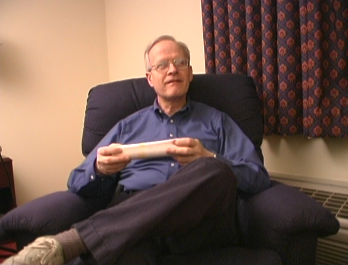 Ward Christensen sits in an easy chair, smiling to the camera as he replies to an interviewer off-camera.