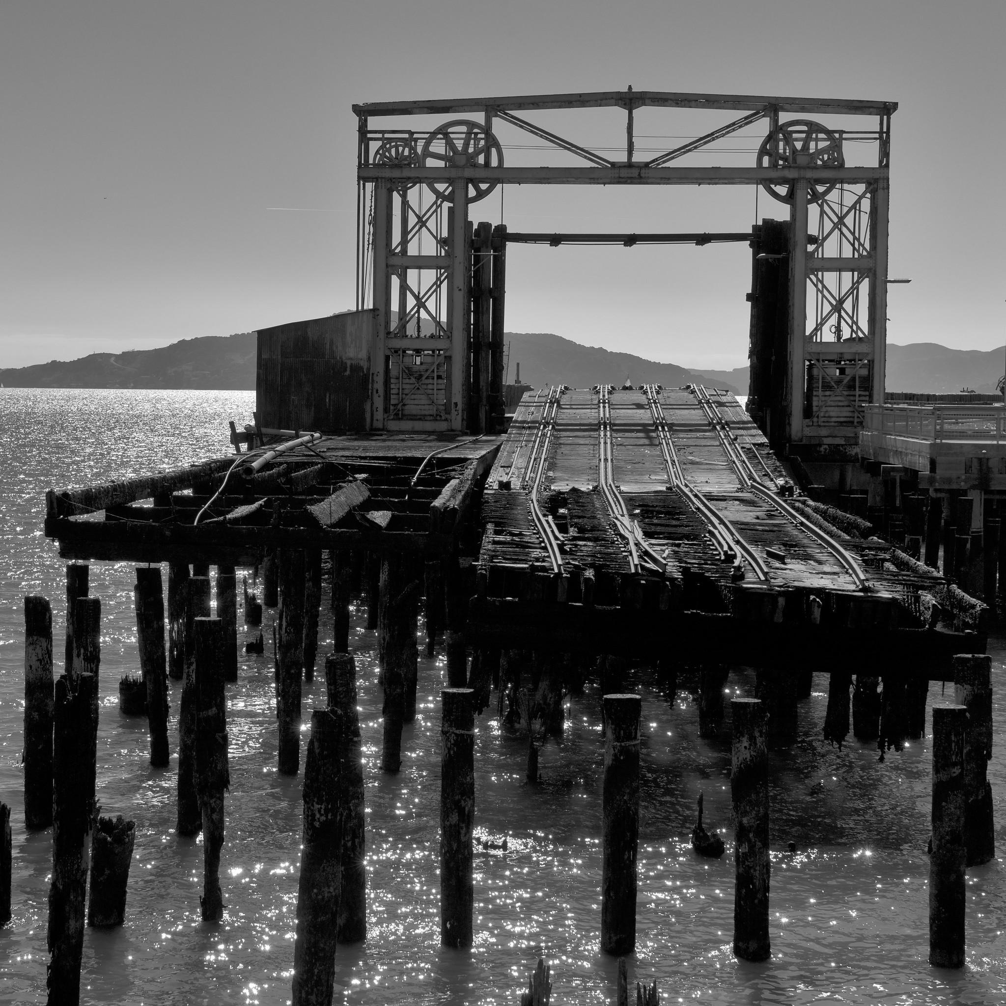 Charred ties and tracks on a pier, with hills in background.