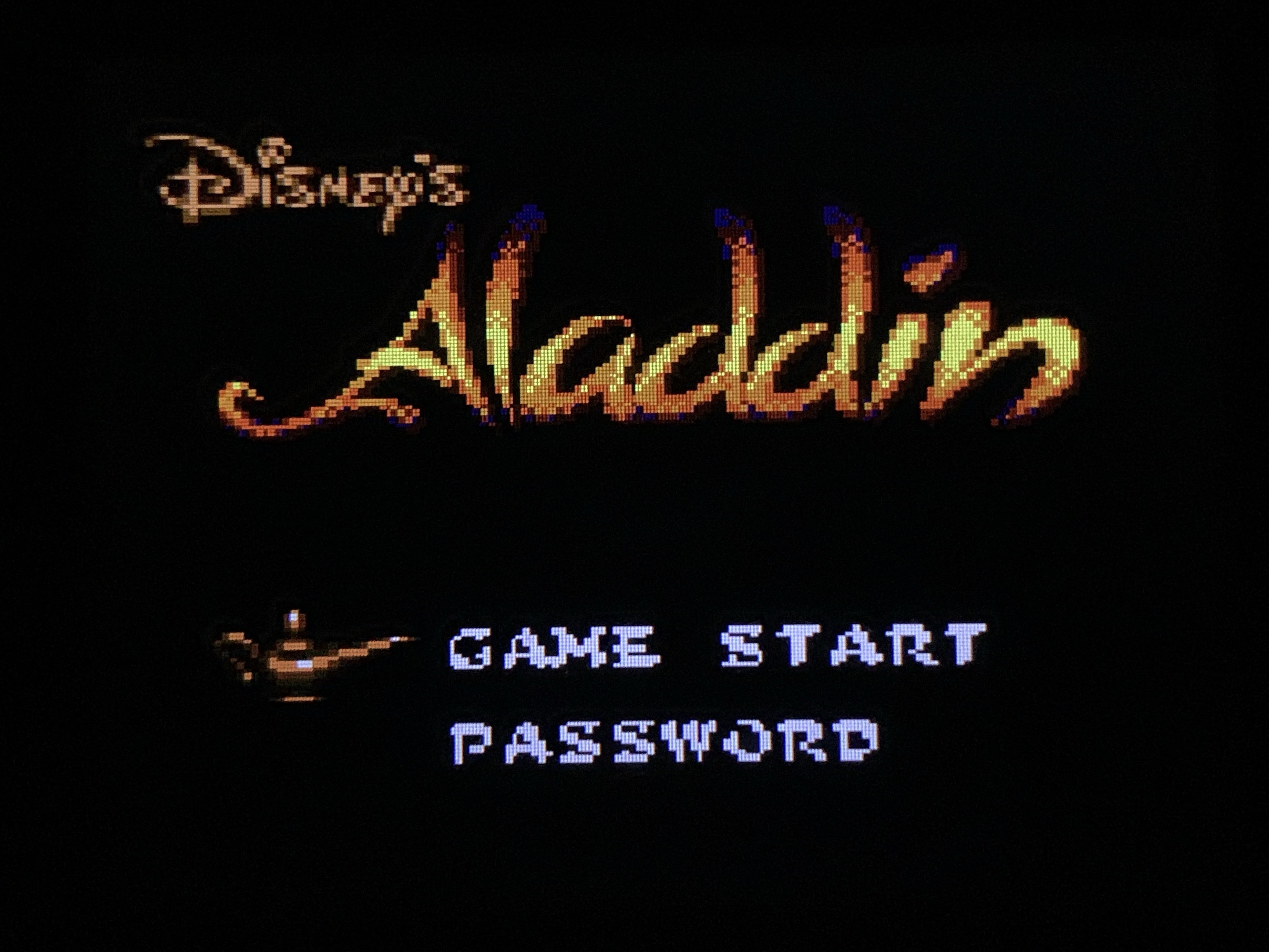 The image shows the title screen of Disney's "Aladdin" video game. It features the game's title in stylized text with options for "GAME START" and "PASSWORD" below. An image of a magic lamp is displayed next to the text