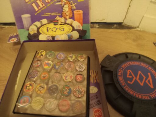 Pog the game box with a book full of pogs. To the side is a pog arena