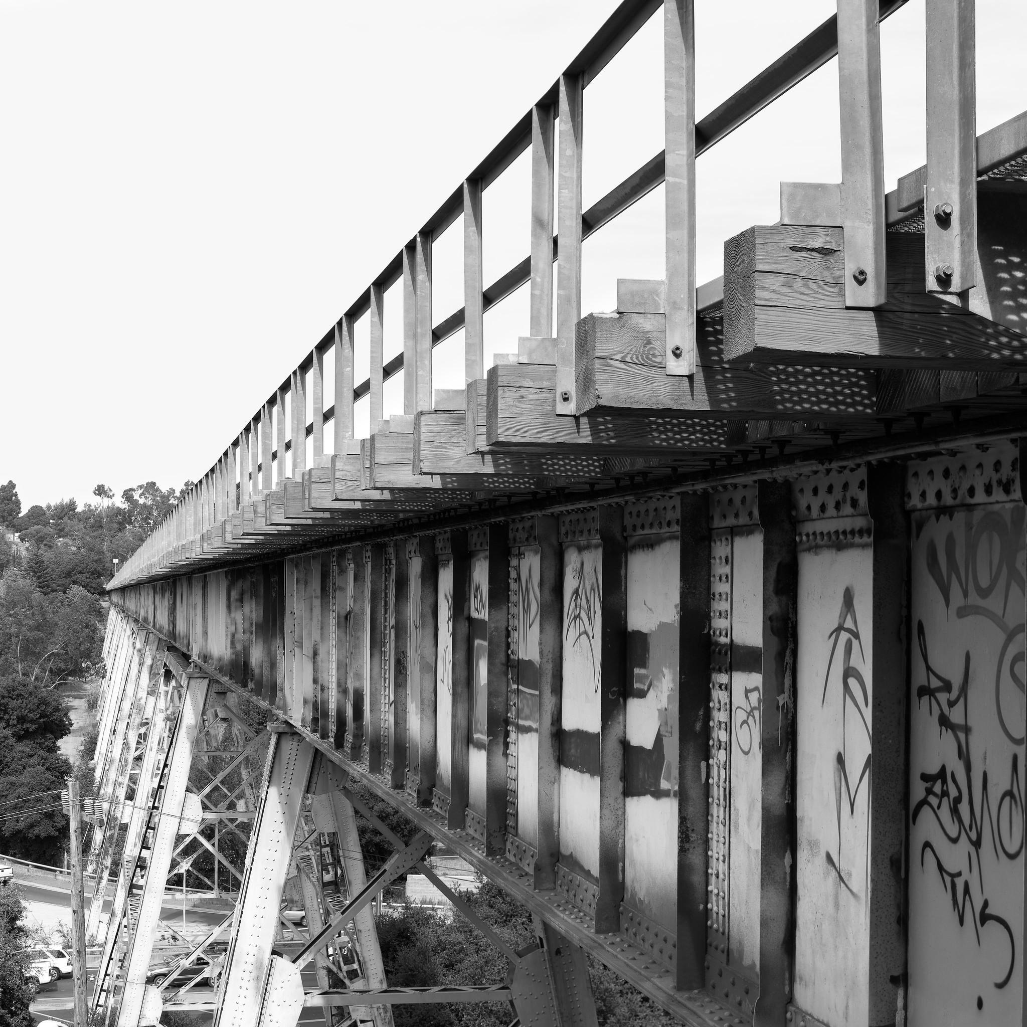 A tall steel railroad trestle over a highway, converging at the left of the frame. There's graffiti on the side of the trestle.