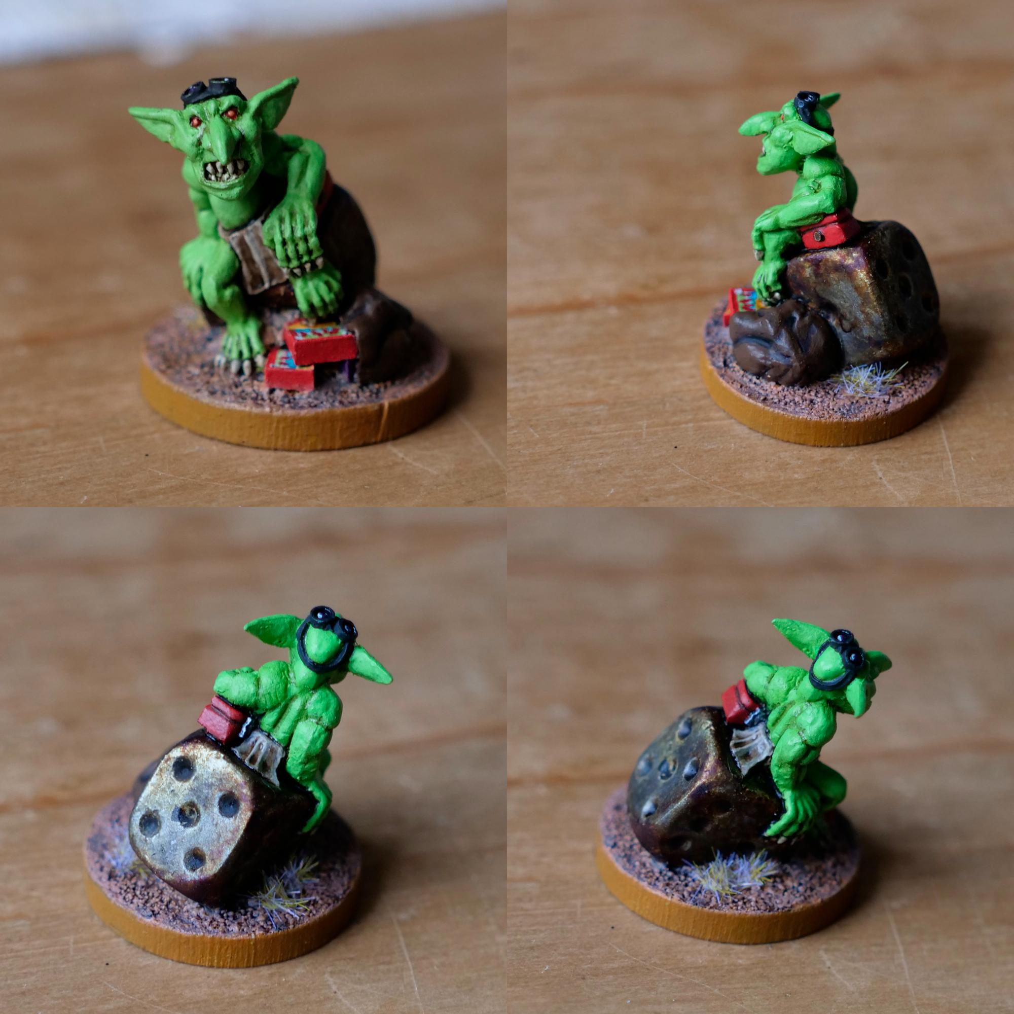 Four shots of the same wargaming miniature (different angles). The sculpt is of a goblin, sat on a dice (painted to look rusty), with a bag at his feet spilling out boxes (painted to look like the boxes Warhammer miniatures came in the mid 1990s). The goblin is wearing a loin cloth and leaning on a small, red money box (the lockable kind often used by traders running stalls at conventions).  The goblin is about an inch tall and there's small tufts of dried grass on the base of the model.