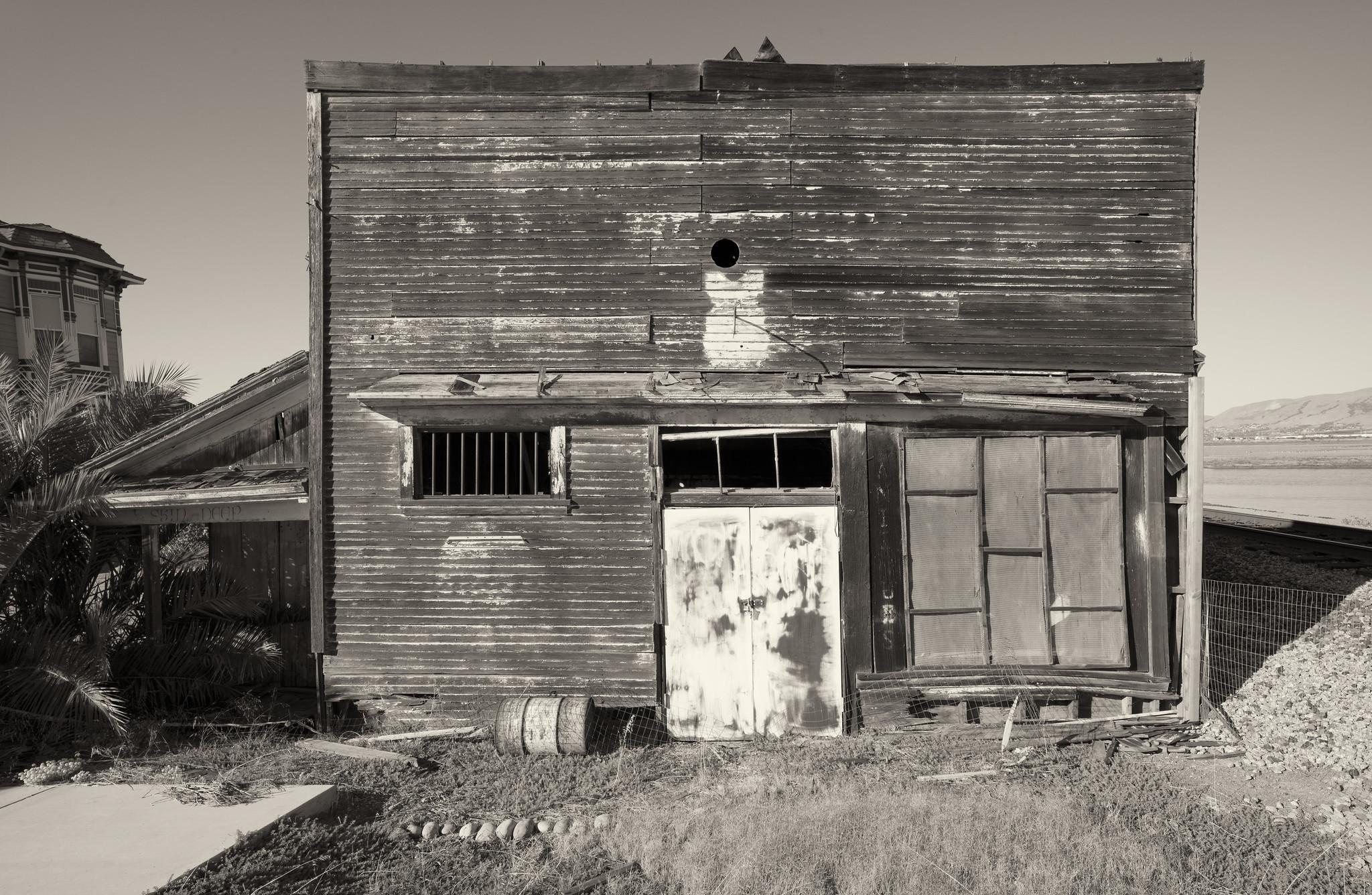 A disused, dilapidated clapboard storefront, with windows and doors boarded up.